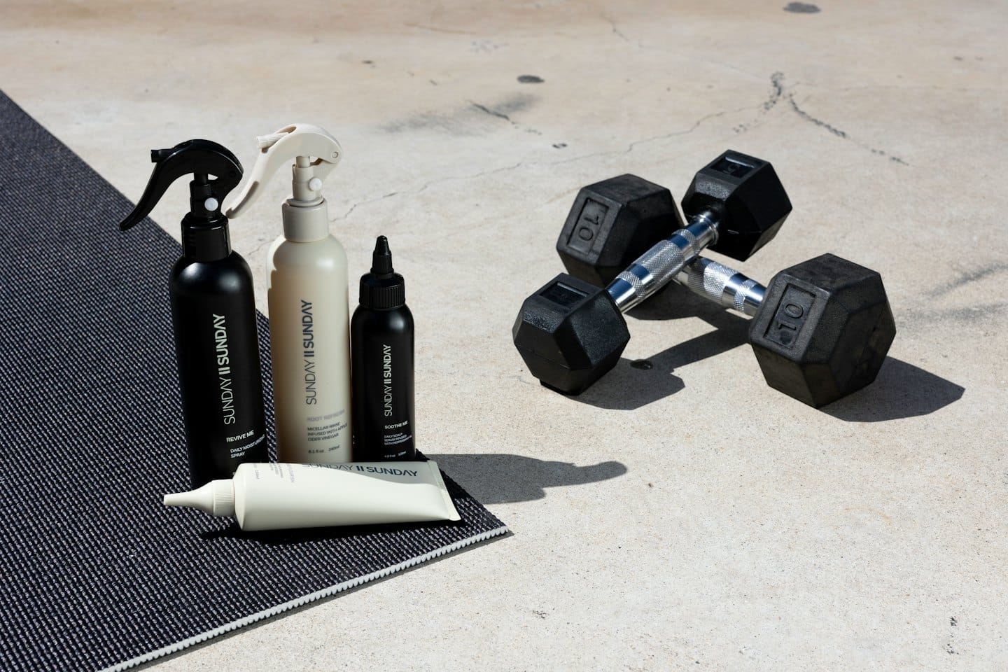 Four branded hair care products and dumbbells on a mat.