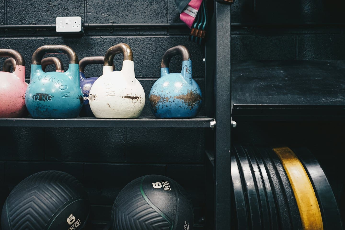 Gym equipment including kettlebells and weights on shelves.